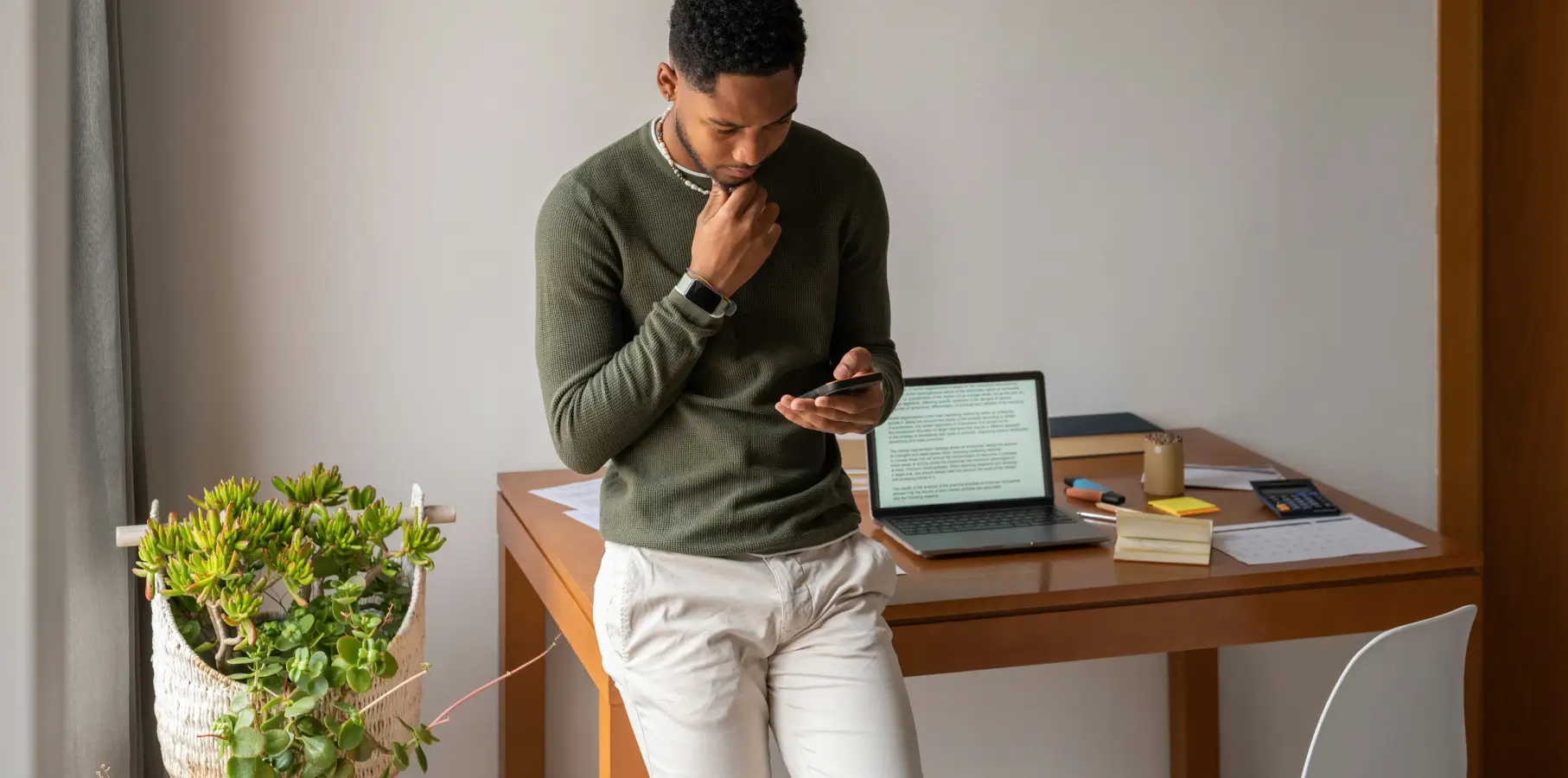 Person looking at their phone while leaning on a desk with a laptop open on it